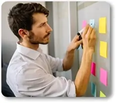 Hombre joven escribiendo notas de colores sobre una pizarra